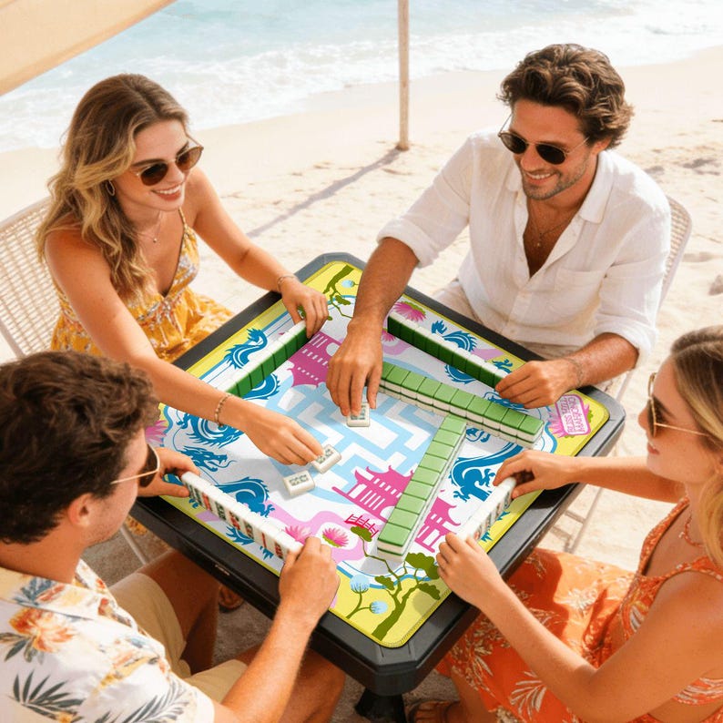 May include: A square Mahjong game table with a colorful design featuring dragons, pagodas, and floral elements. The table is surrounded by four people playing the game on a beach setting. The game pieces are white and green.