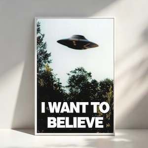 Peut inclure: Une affiche encadrée représentant un OVNI au-dessus d'une forêt. L'image a une esthétique vintage. Le texte blanc en gras en bas dit "I WANT TO BELIEVE". L'affiche est présentée contre un mur blanc.