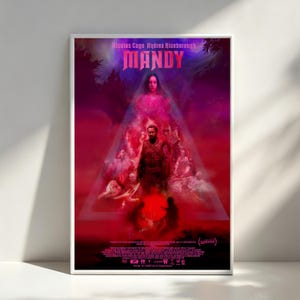 May include: A framed movie poster for "Mandy" featuring Nicolas Cage and Andrea Riseborough. The poster has a dark, red and purple color scheme with the title in bold, stylized letters. The image includes a central figure and other characters.