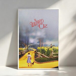May include: A framed poster featuring The Wizard of Oz with a person in a blue dress and a small dog walking on a yellow brick road. A scarecrow stands in a cornfield beside a white fence under a hazy sky with the movie title in red text.