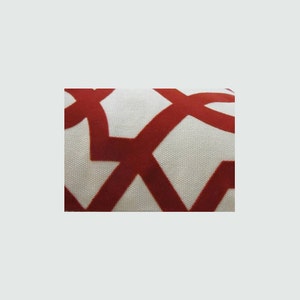 Op de afbeelding: Close-up van een witte stof met een rood geometrisch patroon. Het patroon bestaat uit in elkaar grijpende cirkels en vierkanten.
