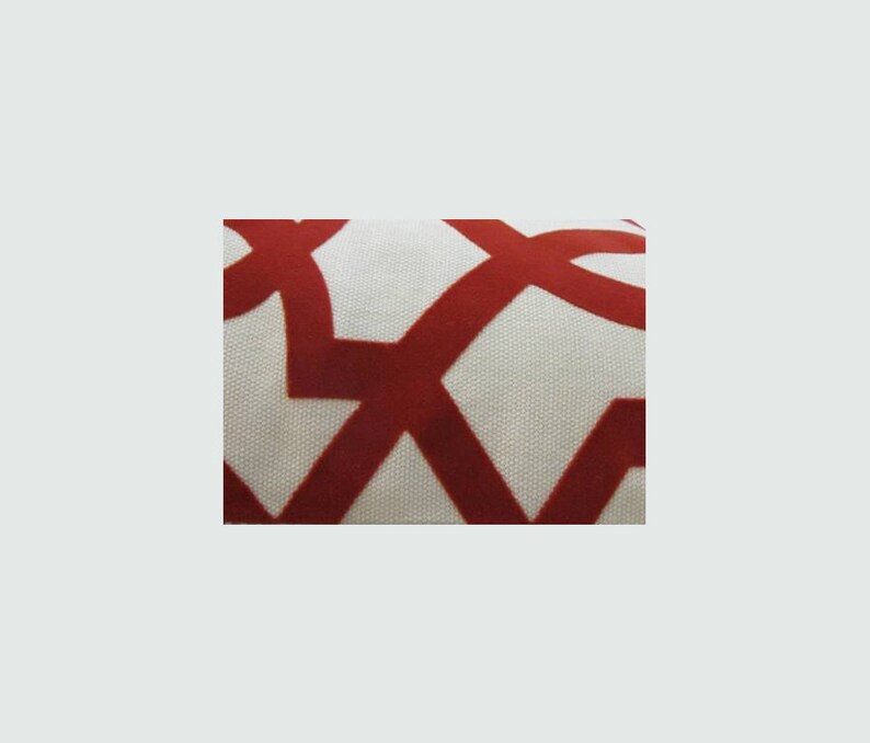 Op de afbeelding: Close-up van een witte stof met een rood geometrisch patroon. Het patroon bestaat uit in elkaar grijpende cirkels en vierkanten.
