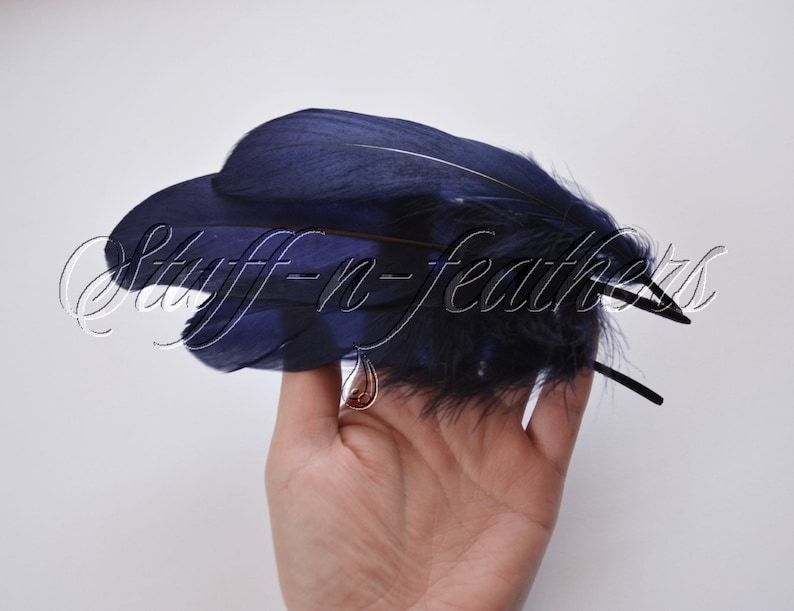 May include: A cluster of dark blue feathers with a black wire stem. The feathers are arranged in a fan shape and are held in a hand.