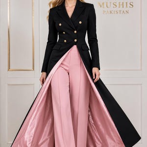 Puede incluir: Una chaqueta larga negra de doble botonadura con botones dorados y forro de satén rosa, combinada con pantalones anchos rosas a juego. La prenda presenta una solapa estructurada y un diseño frontal abierto, con el texto M MUSHIS PAKISTAN visible.