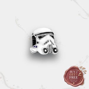 May include: A silver charm bead shaped like a Star Wars Stormtrooper helmet, featuring white enamel detailing, black accents on the eyes and mouth, and small blue highlights on the side, with the brand name Pandora engraved on the side.