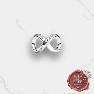 May include: A silver-toned infinity charm featuring the engraved black text "Family" and "Forever and Always" along its curved surface. The charm has a smooth, polished metallic finish and a continuous looped design representing the infinity symbol.