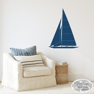 May include: A blue sailboat silhouette wall decal, shown on a white wall above a cream-colored armchair with pillows. The decal is a simple design with a single sail and a hull.