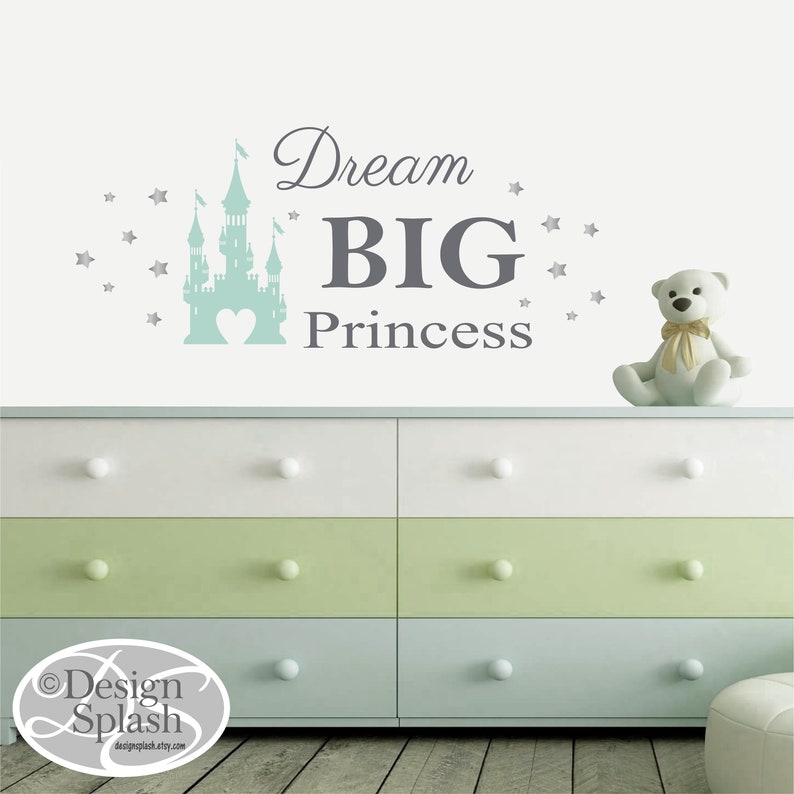 May include: A light blue castle silhouette with a heart in the center, surrounded by silver stars. The text "Dream BIG Princess" is written in gray below the castle.
