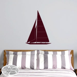 May include: A maroon sailboat wall decal on a white striped bedspread. The decal is a silhouette of a sailboat with a single mast and a large sail.