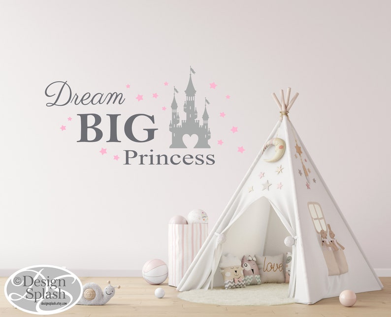 May include: A white teepee tent with pink stars and a crescent moon design. The teepee is set up in a room with a gray wall and a pink and white striped storage bin. A gray castle silhouette with a pink heart is on the wall with the text "Dream BIG Princess" in gray.