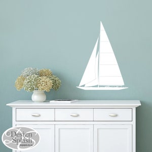 May include: White sailboat wall decal on a light blue wall above a white dresser with three drawers. The dresser has two doors on the bottom. A vase with white and green flowers sits on top of the dresser.