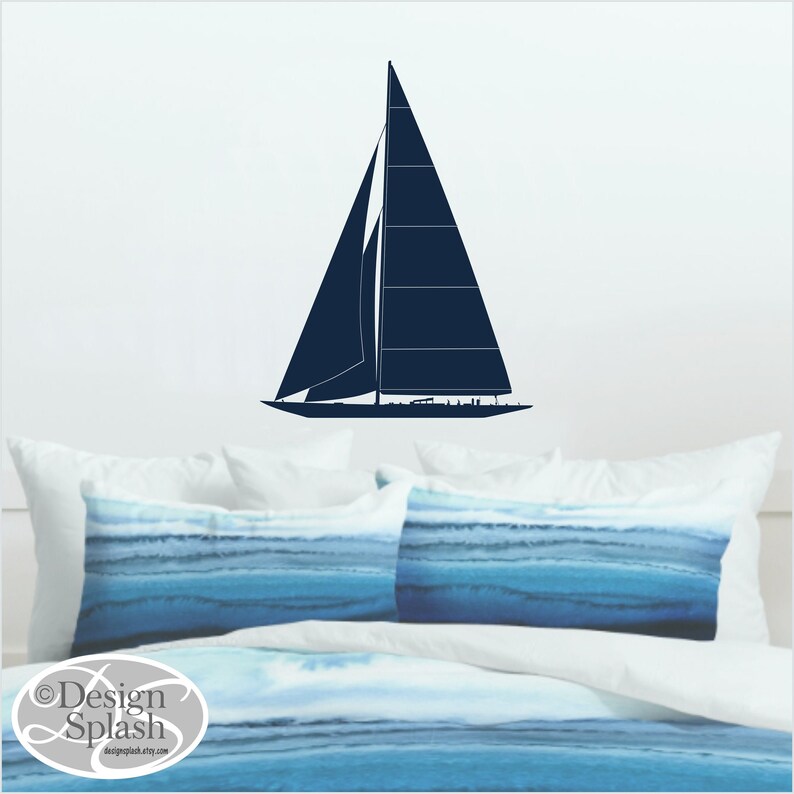 May include: A dark blue sailboat silhouette wall decal on a white wall above a bed with blue and white bedding.