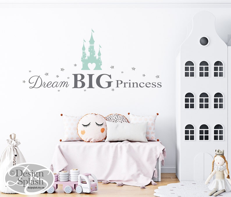 May include: A light green castle silhouette with a heart in the center, surrounded by small silver stars. The text "Dream BIG Princess" is written below the castle in gray.