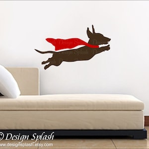 May include: A brown dachshund wearing a red cape, flying through the air. The dog is silhouetted against a white wall. The image is a graphic design for a wall decal.
