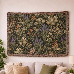 Peut inclure: Un plaid tissé rectangulaire présentant un fond vert foncé avec un motif botanique dense composé de diverses fleurs, de feuilles vertes et de petits fruits ronds. Les bords du plaid sont finis avec une bordure à franges décorative.