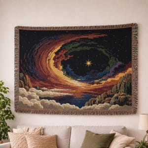 Peut inclure: Une tapisserie tiss&eacute;e rectangulaire repr&eacute;sentant une sc&egrave;ne nocturne c&eacute;leste avec une &eacute;toile centrale brillante, des nuages tourbillonnants color&eacute;s dans des tons orange, violet et bleu, et des sommets rocheux au-dessus de nuages blancs.