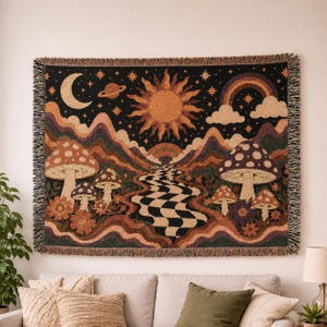 Peut inclure: Une tapisserie tissée représentant un paysage fantaisiste avec des champignons, un chemin en damier et des éléments célestes. La palette de couleurs comprend des nuances de marron, d'orange et de noir, avec une bordure à franges. La tapisserie est accrochée au mur au-dessus d'un canapé.