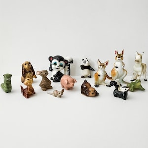May include: A collection of small ceramic animal figurines, including a monkey, panda, kangaroo, dog, and pig. The figurines are painted in various colors and styles, with some featuring detailed designs.