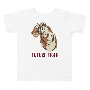 May include: White toddler t-shirt featuring a tiger illustration in shades of brown and cream. The words "FUTURE TIGER" are printed in burgundy below the tiger graphic. The shirt is made of a soft, comfortable material.