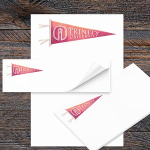 May include: White sticky notes with a Trinity University pennant design. The pennant is pink and red with the university's name and logo. The image is on a wooden background.