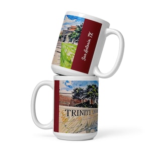 May include: Two white ceramic mugs stacked on top of each other. The top mug features a watercolor painting of a building and the text "San Antonio, TX" on a burgundy stripe. The bottom mug displays "TRINITY UNIVERSITY" and a watercolor painting.