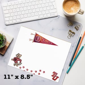 May include: A white sheet of paper with a Trinity University pennant, tiger mascot, and paw prints. The paper measures 11" x 8.5". A keyboard, coffee, and pencils are in the background.