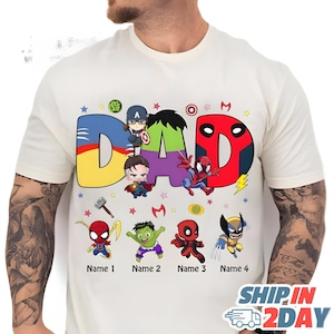 May include: Cream-colored t-shirt with the word "DAD" in large, colorful letters, each letter designed with a superhero theme. Below the word are cartoon superhero characters and spaces for names.