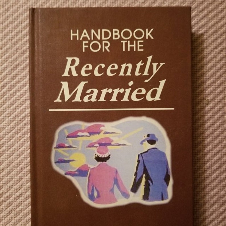 May include: A brown book with the title "Handbook for the Recently Married" in white text. The cover features a cartoon illustration of a couple walking hand-in-hand in front of a sun and clouds.
