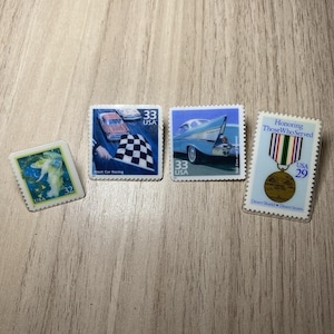 Puede incluir: Cuatro sellos postales con diseños diversos: un sello de 32 centavos con un ángel azul, uno de 33 centavos de carreras de autos con una bandera a cuadros, uno de 33 centavos con la aleta trasera de un auto azul y uno de 29 centavos conmemorativo.