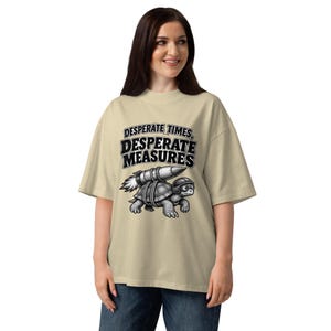 May include: A beige short-sleeve t-shirt featuring a black and white graphic of a turtle wearing a helmet and goggles with a rocket strapped to its shell. The text above the turtle reads, "DESPERATE TIMES, DESPERATE MEASURES" in bold black letters.