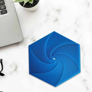 May include: A blue hexagonal coaster with a spiral design. The coaster is made of a ridged material and is approximately 4 inches wide. The coaster sits on a white marble surface.