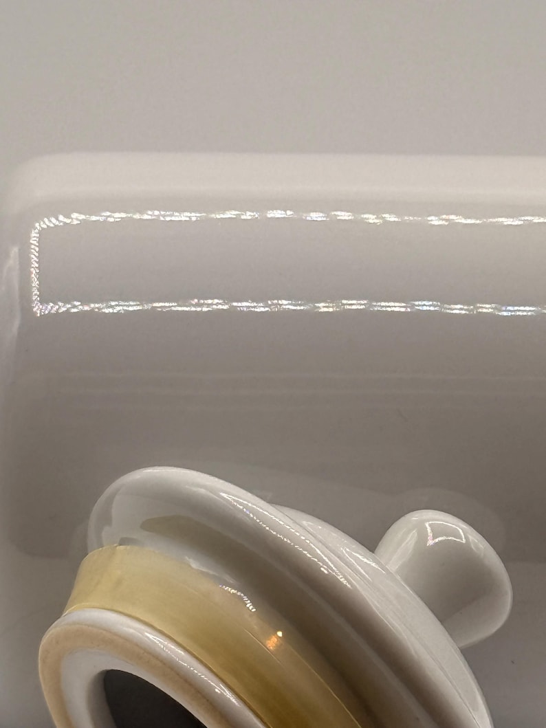 Puede incluir: Una mantequera de cer&aacute;mica blanca con tapa y asa. La tapa tiene forma curva y un asa peque&ntilde;a. El plato tiene forma rectangular. El interior del plato es de color amarillo claro.