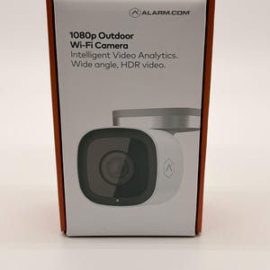 Może przedstawiać: Białe, prostokątne opakowanie produktu kamery zewnętrznej Wi-Fi 1080p Alarm.com. Pudełko zawiera logo Alarm.com, nazwę produktu oraz tekst Intelligent Video Analytics i Wide angle, HDR video wraz z grafiką przedstawiającą kamerę.