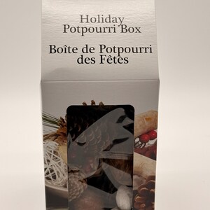 Può includere: Una scatola rettangolare in cartone bianco con l'etichetta Holiday Potpourri Box e Boîte de Potpourri des Fêtes. La parte anteriore presenta una finestra rettangolare che mostra pigne, bacche rosse e sfere decorative bianche.
