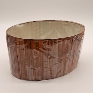 May include: An oval-shaped lampshade featuring a dark brown wood grain pattern on the exterior. The shade is wrapped in a clear protective plastic film. The interior of the lampshade is lined with a smooth, off-white material.