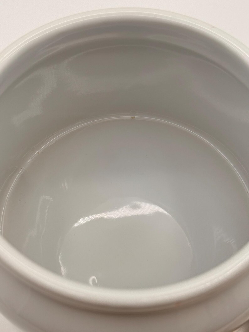 May include: A white ceramic bowl with a smooth, glossy interior finish and a rounded rim. The bowl features a deep, open basin with a curved base, reflecting light on its polished surface. The design is simple, functional, and uniform in color.