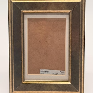 May include: A rectangular picture frame with a dark, mottled grey finish and gold-toned edges. The frame features a white mat board surrounding a brown backing. A white label on the backing displays the text VIRSERUM 22509 and IKEA.