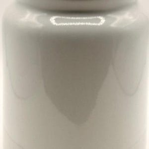 Puede incluir: Un tarro de cer&aacute;mica blanco con tapa. El tarro tiene un cuerpo cil&iacute;ndrico y una base ligeramente m&aacute;s ancha. La tapa se asienta al ras en la parte superior. La superficie del tarro es lisa y brillante, reflejando la luz. El dise&ntilde;o general es simple y minimalista.