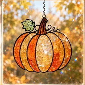 May include: A stained glass pumpkin suncatcher featuring orange and yellow textured glass segments outlined in black metal. The pumpkin has a dark orange stem, a single green leaf, and a metal chain for hanging in a window to catch light.