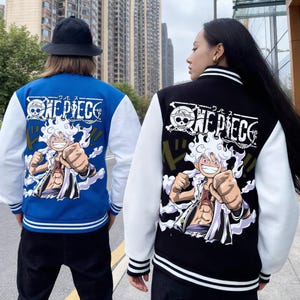 May include: Two varsity jackets, one blue and one black, both featuring white sleeves and ribbed cuffs with white stripes. The back of each jacket displays a large graphic of a smiling anime character with white hair and the text ONE PIECE.