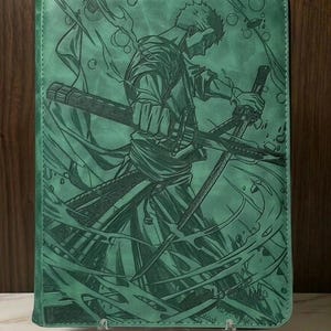 Puede incluir: Una carpeta portafolio rectangular de color verde menta con un grabado láser detallado de un espadachín sosteniendo tres espadas katana. La ilustración muestra una escena dinámica con líneas fluidas y burbujas, con una cremallera plateada.