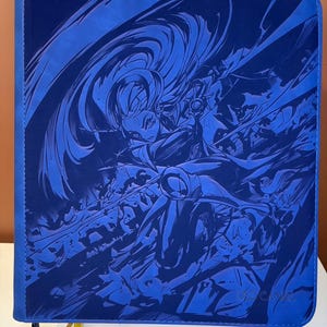 Könnte beinhalten: Ein quadratischer blauer Ringordner mit Reißverschluss, der eine monochrome dunkelblaue grafische Illustration einer dynamischen Figur mit wehendem Haar in Kampfpose zeigt. Der Einband hat eine glatte Textur mit einem Reißverschluss an der linken Seite.