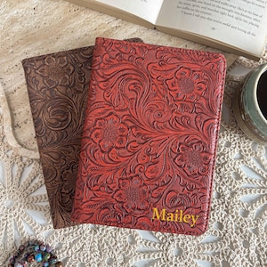 May include: Two rectangular book covers with an embossed floral pattern. One cover is dark brown, and the other is a vibrant red with the name Mailey printed in yellow text at the bottom right corner. Both covers are placed on a white lace surface.