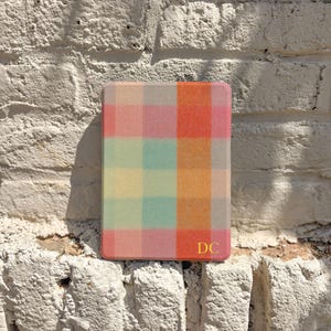 May include: A rectangular e-reader case featuring a multicoloured plaid pattern in shades of orange, pink, yellow, and teal. The bottom right corner of the case displays the gold-coloured initials DC printed in a clean, sans-serif font.