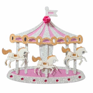 May include: A white and pink glitter carousel with three white horses and a pink flower on top. The carousel is made of paper and has a gold trim.