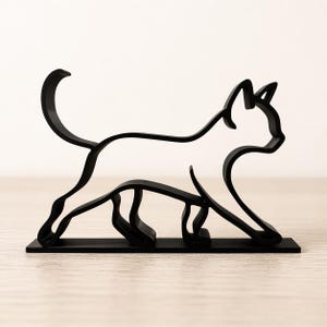 May include: A black metal cat sculpture in a walking pose. The cat's form is defined by a continuous line, creating a minimalist and modern aesthetic. The sculpture is mounted on a rectangular base.