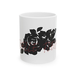 May include: White ceramic mug featuring a black rose design with leaves and the text "BELLE FLEUR" in red cursive. The mug is cylindrical and suitable for hot or cold beverages.