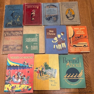 May include: A collection of eleven vintage children's hardcover books with illustrated covers. Titles include Play Fellows, Fifty Flags, Good Reading, Story Hour Readers Primer, The Primer, Sunshine and Rain, We Three, Busy Days with Little Friends, Merry Go-Round, Open the Gate, and Round About, featuring various colorful graphic designs.