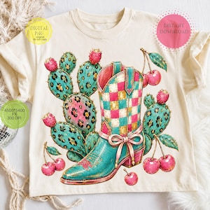 May include: A cream-colored t-shirt featuring a graphic print of a turquoise and pink checkered cowboy boot surrounded by leopard-print cacti with pink fruit and clusters of bright red cherries. The design includes a pink bow on the boot.