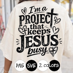 Puede incluir: Camiseta color crema con el texto negro "I'm a PROJECT that keeps JESUS busy". El diseño incluye corazones, una cruz y las palabras "PNG SVG 2 colors" en círculos negros.